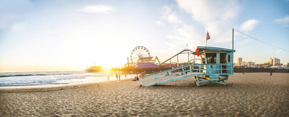 Santa Monica Pier in the background. Life guard tower, with people walking on the beach during sunset.