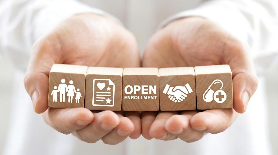 Open enrollment wooden blocks held in hands representing health insurance and medical benefits for family coverage.