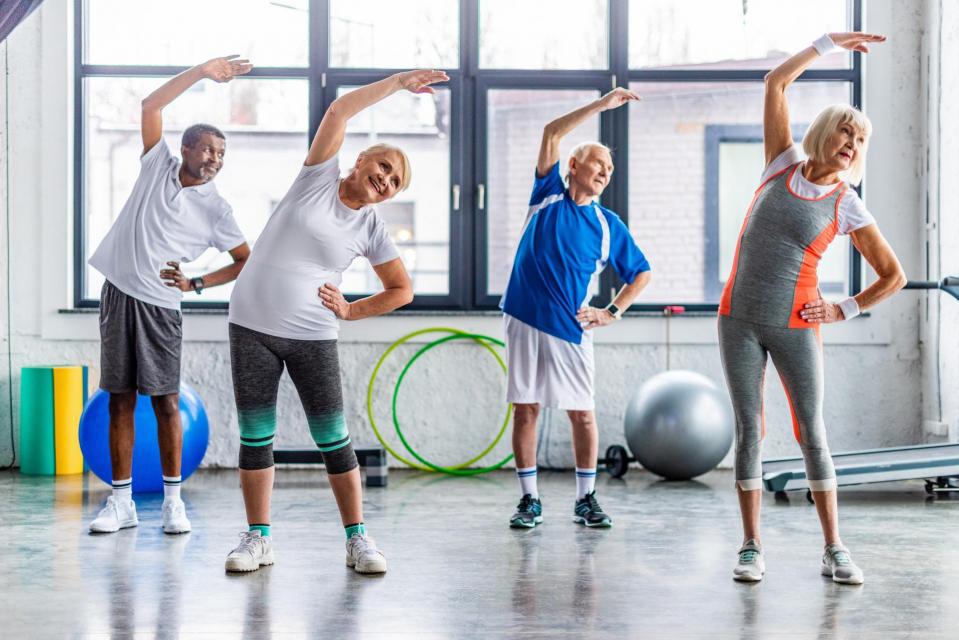 happy multiethnic senior sportspeople synchronous exercising at sports hall