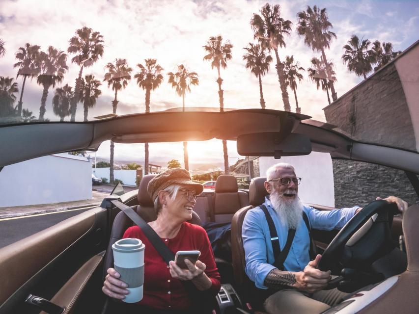 Trendy senior couple in a convertible with sunset background.
