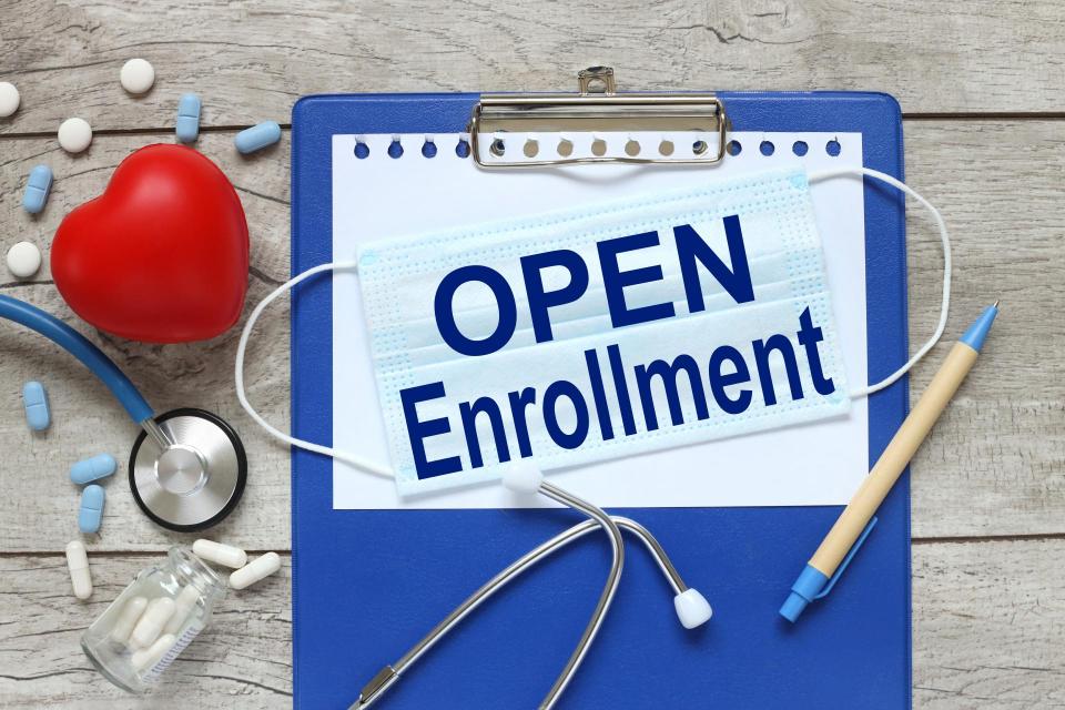 Open Enrollment. Stethoscope with notepad, red heart and pen on blue wooden table