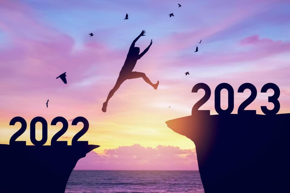 Silhouette man jumping between cliff with number 2022 to 2023 and birds flying at top of mountain