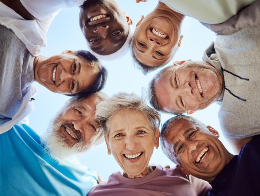 Seven adults arranged in a close circular connecting  huddle, faces pointing inward toward the camera expressing joy.