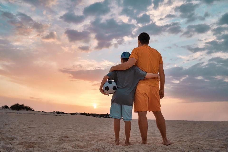 Father and Son playing football, family fun outdoors players in soccer in dynamic action have fun playing football in the beach