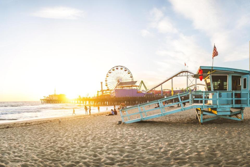 Santa Monica Pier in the background. Life guard tower, with people walking on the beach during sunset.