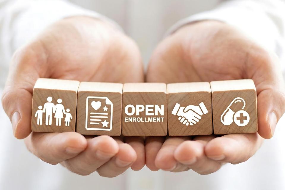 Open enrollment wooden blocks held in hands representing health insurance and medical benefits for family coverage.