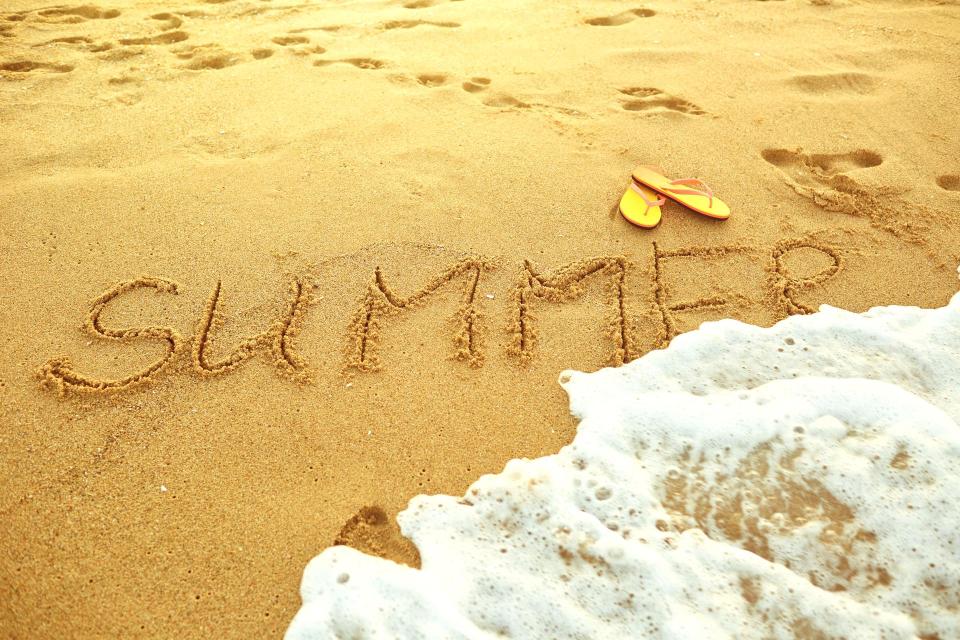 A wave reaching the sand were summer is written in the sand.