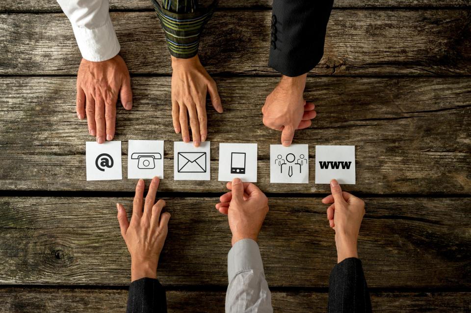 Six people placing white cards with various contact icons in a row.