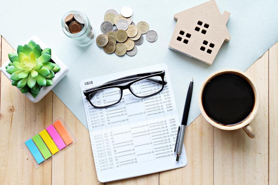 Paperwork, glasses, sticky notes, coins, and a small wooden house on a desk