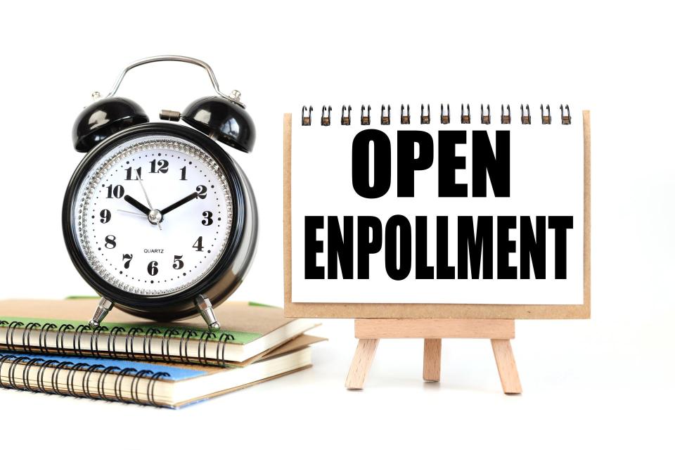 Notepad with Open Enrollment written on it, next to a stack of books and a clock.