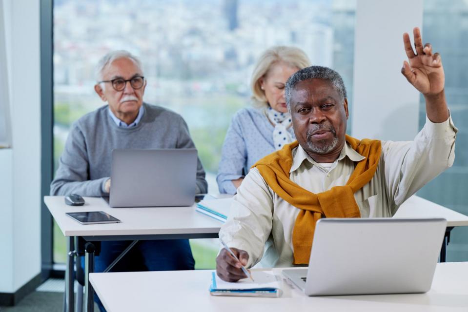 A senior man is working on a laptop while having a training class with a multicultural group of senior people in the classroom.