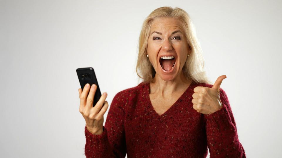 Happy middle aged woman holding smartphone, using mobile applications pointing to phone isolated on white background..