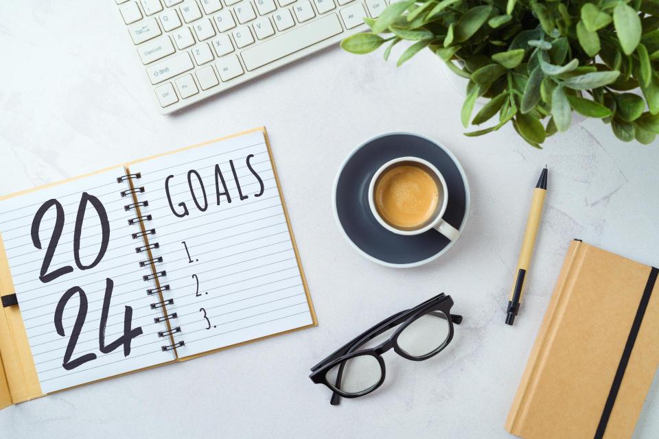 New Year 2024 goals and resolution business concept with notebook, coffee cup, computer keyboard and plant on modern office desk.