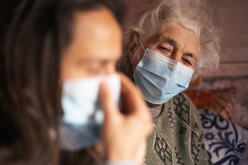 Older woman wearing a medical mask looking at a younger woman also wearing a mask